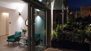 Eine moderne Hotelhalle mit Glastüren, petrolfarbenen Sesseln und einem Tisch mit Blumen.