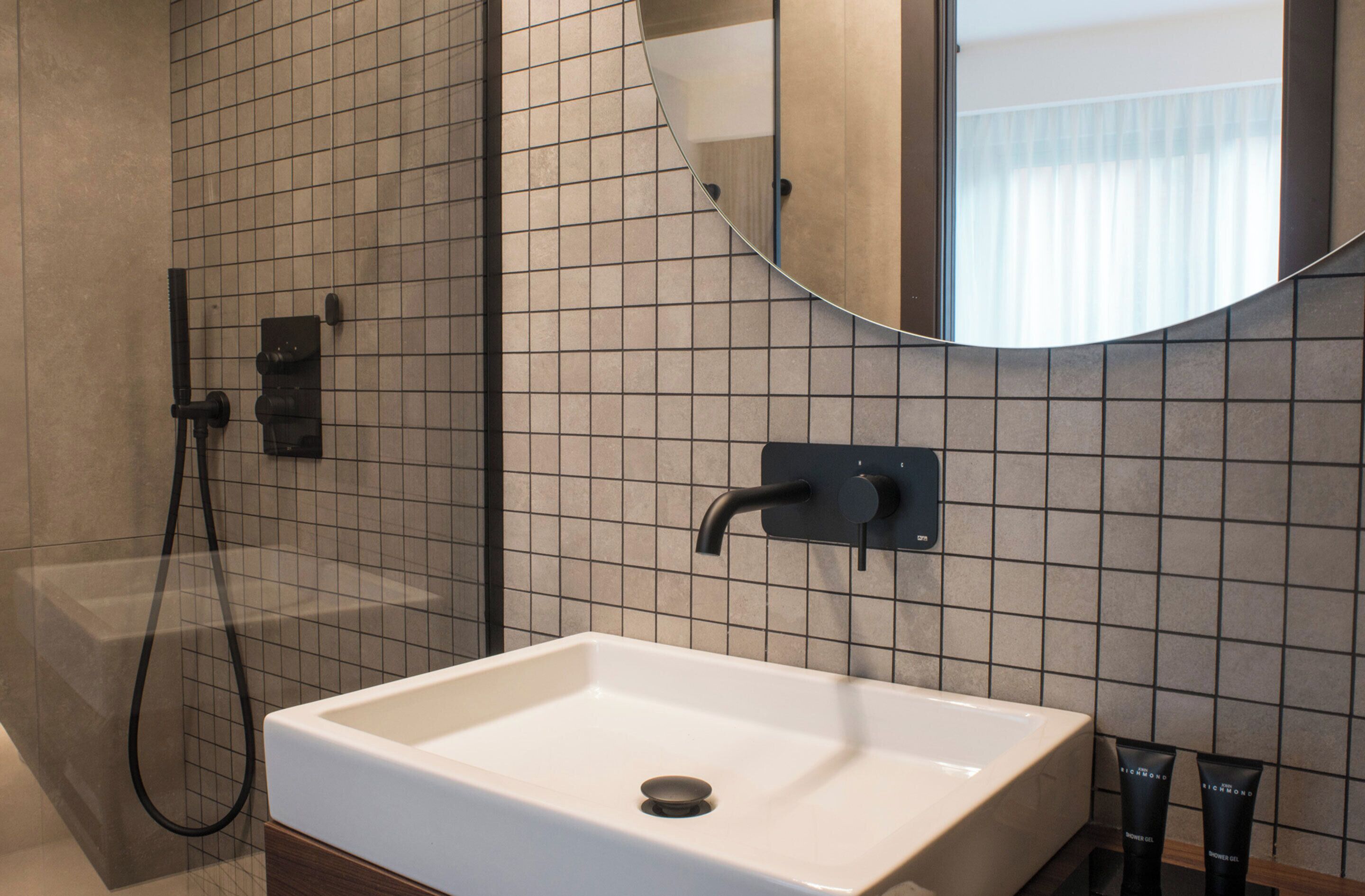 A modern bathroom with a white sink, a handheld showerhead, and a large mirror.