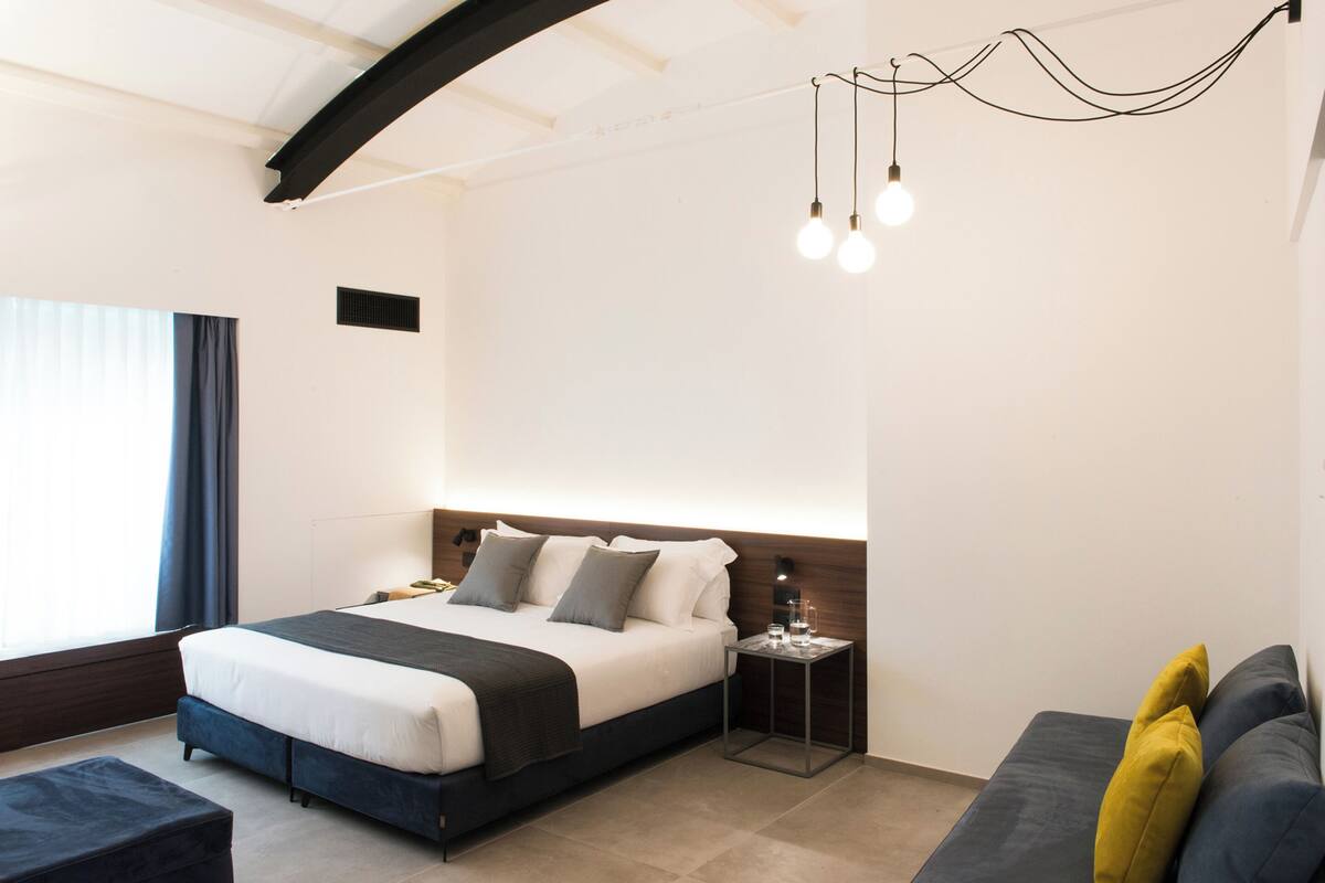 Una habitación de hotel moderna con una cama grande, una mesita de noche y un sofá.
