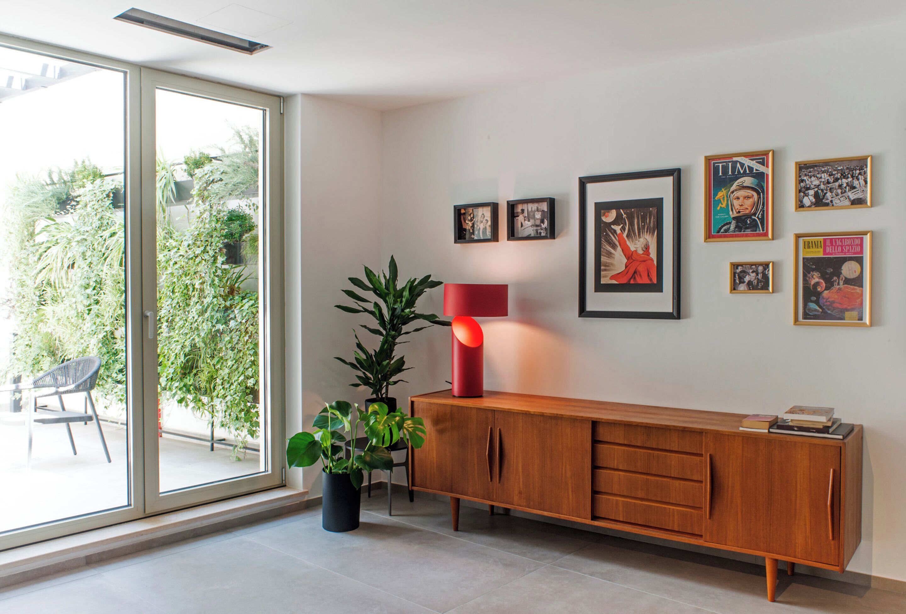 A modern living room with a sliding glass door leading to a balcony, a wooden cabinet with books, and several framed pictures on the wall.