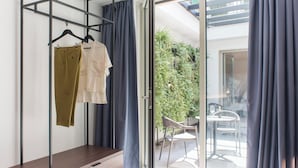 Ein Zimmer mit einer hölzernen Bank, einem Metallgestell mit Kleidung und einer Glastür, die zu einem Außenbereich mit Tisch und Stühlen führt.
