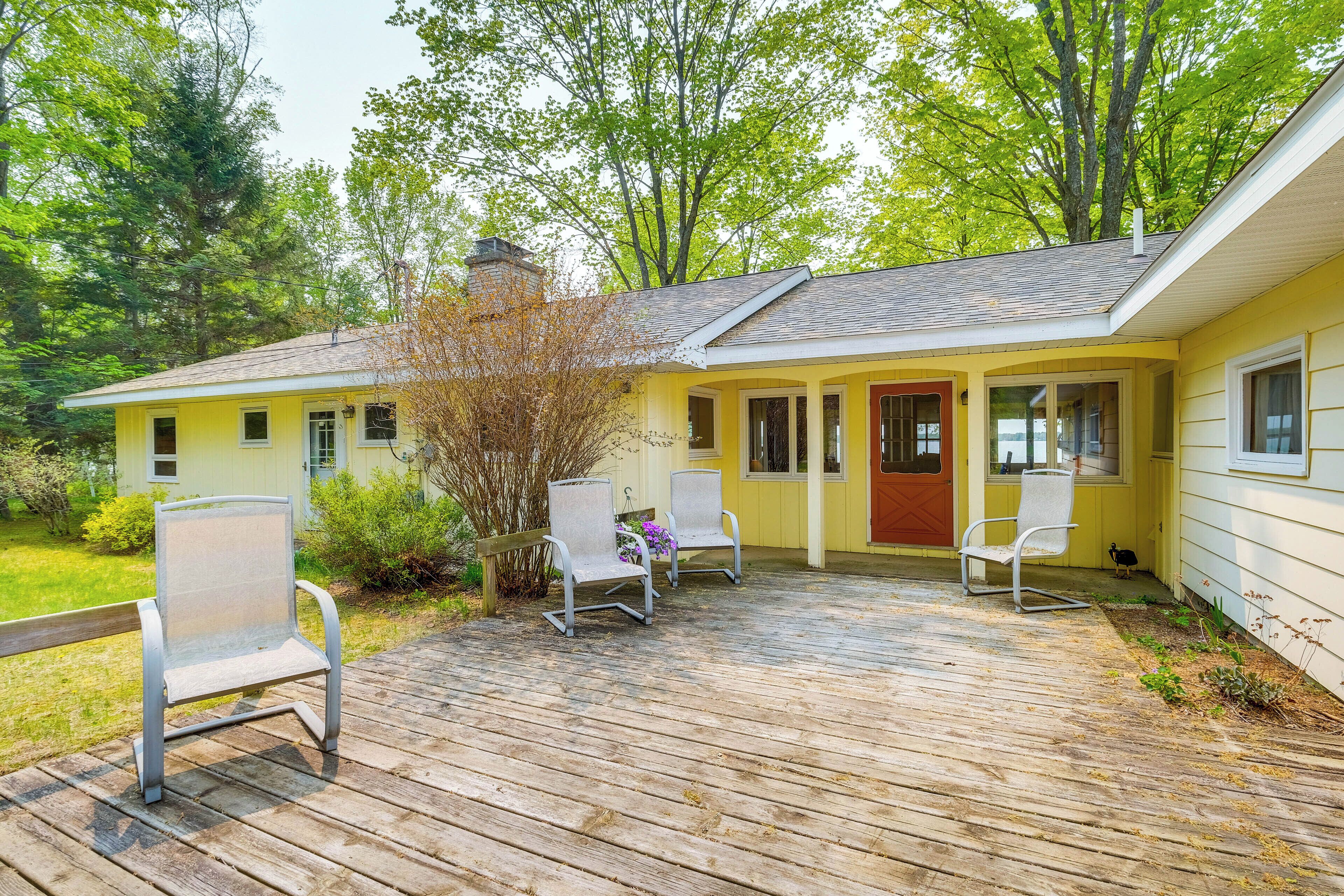 Ein gelbes Haus mit einer Holzterrasse, zwei Stühlen und einer roten Tür.