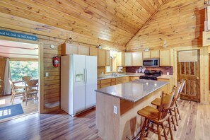 A wooden cabin interior with a kitchen featuring a refrigerator, microwave, and a large island with bar stools. - Secluded Harrison Retreat Near Buffalo Nat’l River (Harrison)