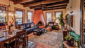 A cozy living room with a fireplace, leather sofa, dining table, and large windows. - Year Around Heated Pool, Mountain Views, Pets Ok (Las Cruces)
