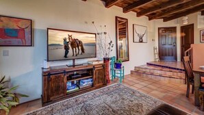 A living room with a large TV, wooden entertainment unit, and a patterned rug. - Year Around Heated Pool, Mountain Views, Pets Ok (Las Cruces)