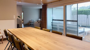 Ett rymligt matområde med ett långt träbord och gula stolar, stora fönster med utsikt över en trädgård och en modern inredning.
