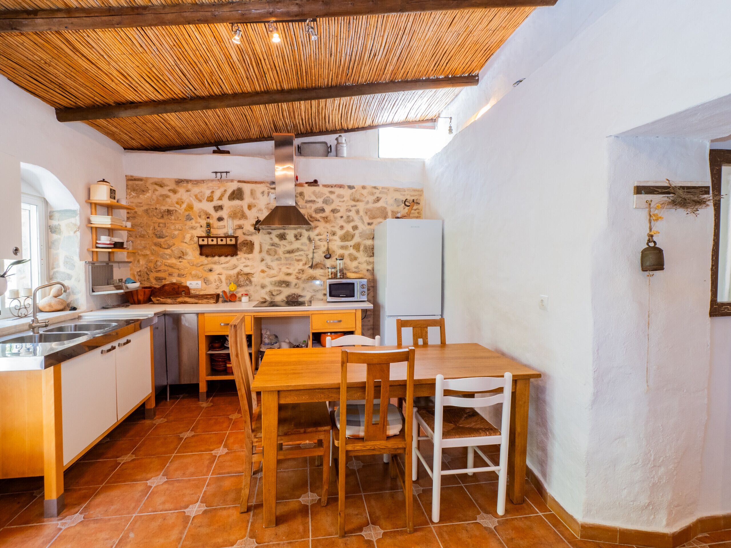 Une cuisine compacte avec un mur en pierre, un plafond en bois et un coin repas comprenant une table et des chaises.