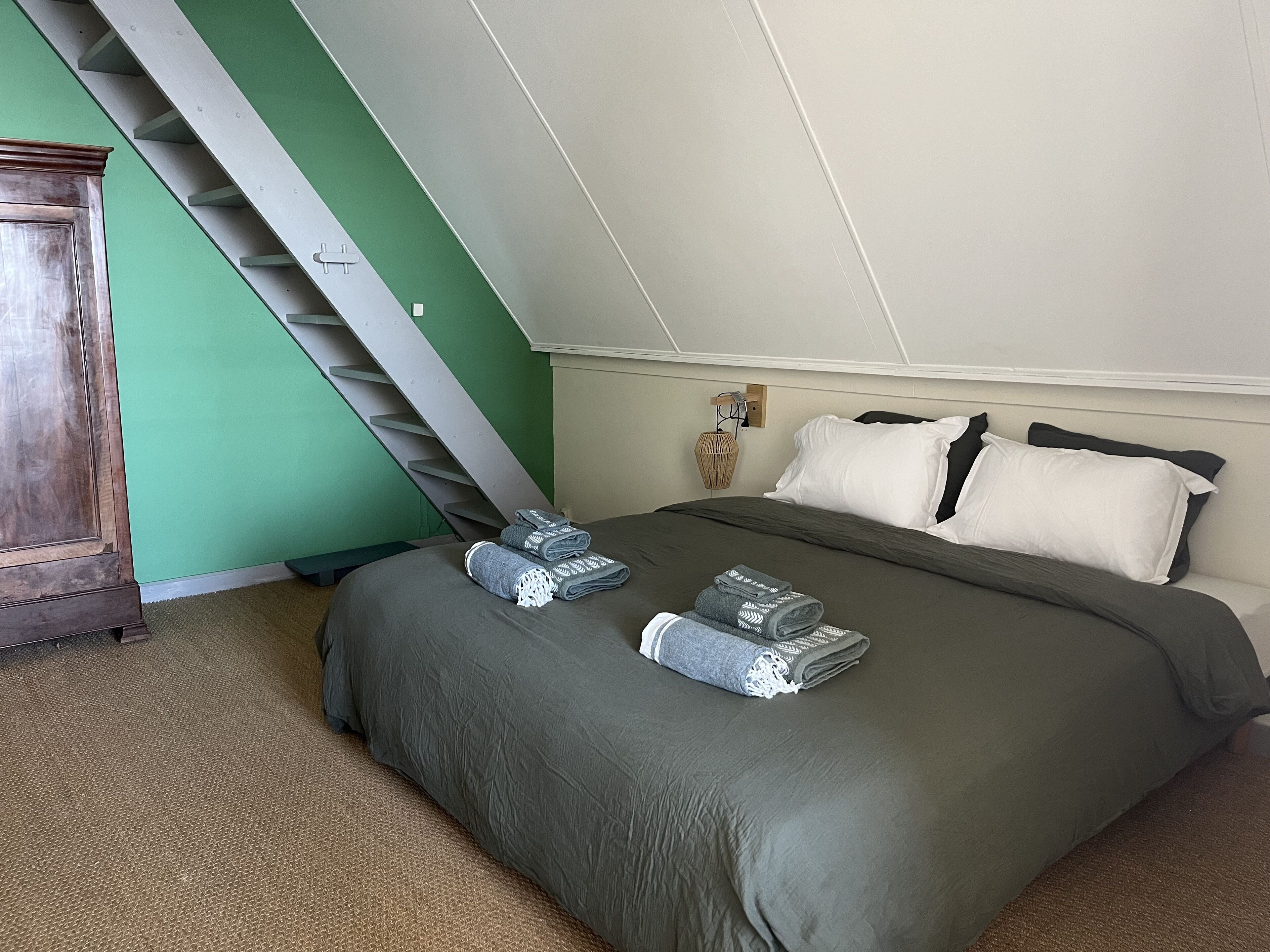 Een slaapkamer met een bed, een nachtkastje, een lamp en een trap.
