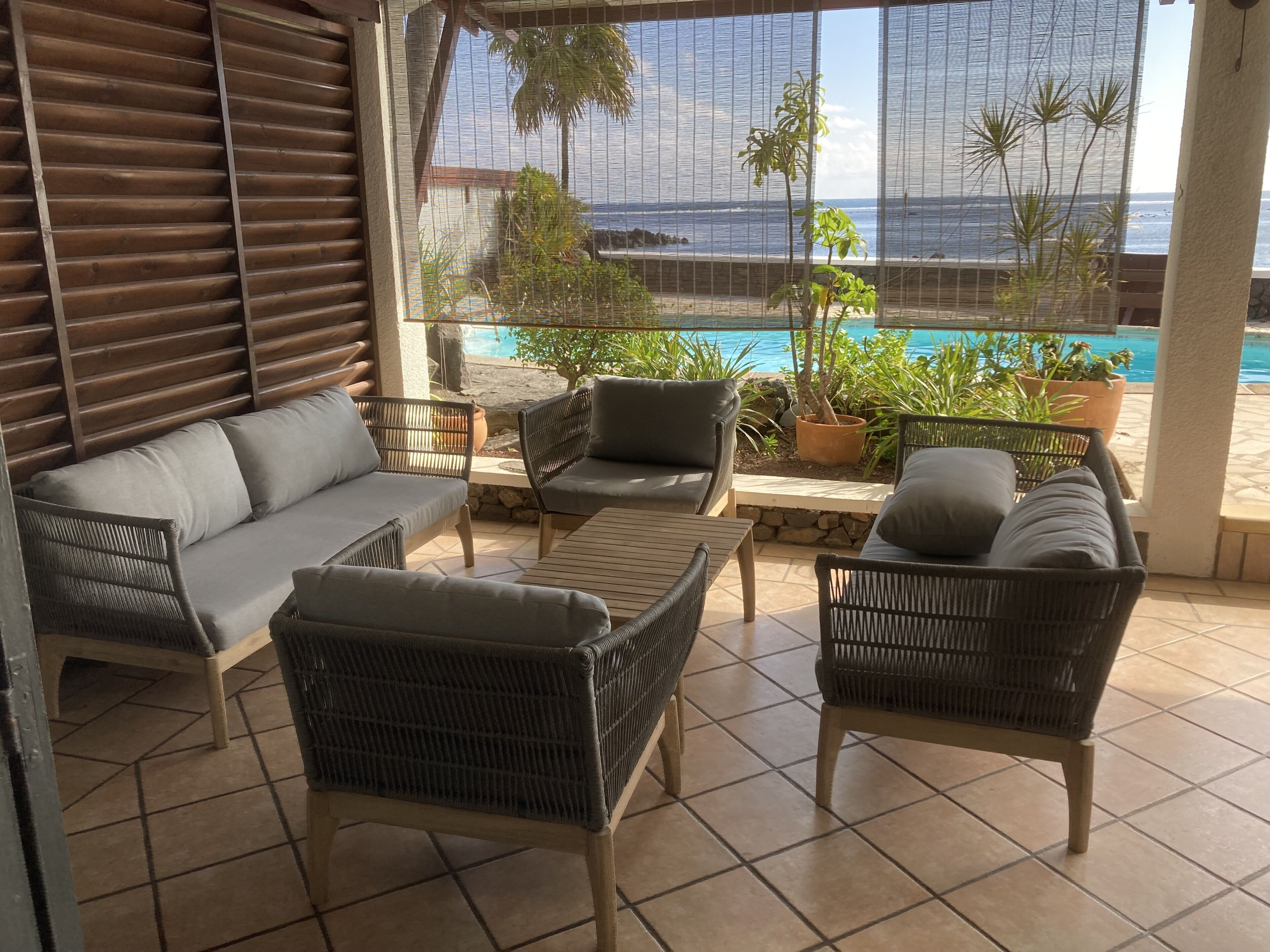 A sunlit patio with wicker furniture, a pool, and a view of the ocean.