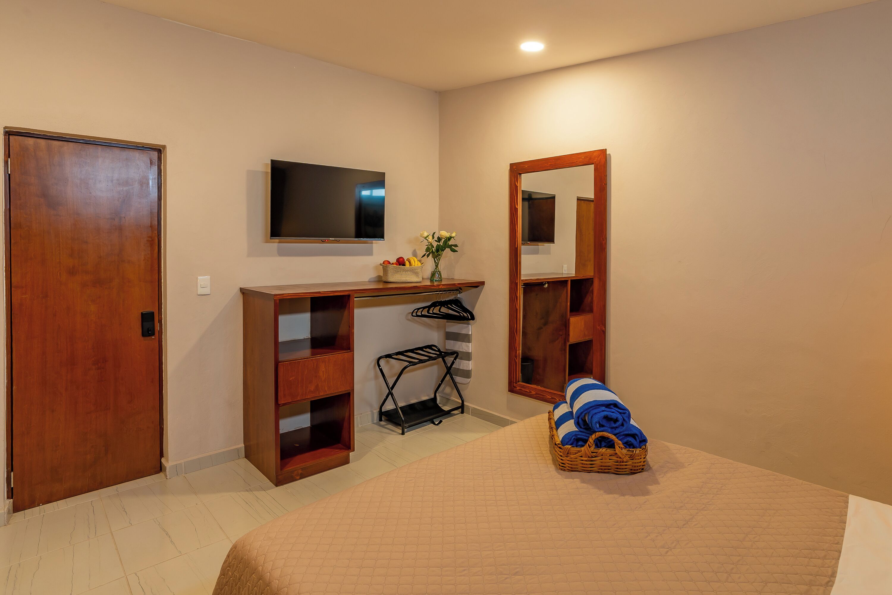 A bedroom with a bed, a wooden desk, a television, a mirror, and a basket of folded clothes.