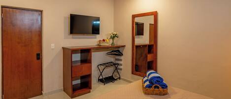 A bedroom with a bed, a wooden desk, a television, a mirror, and a basket of folded clothes.