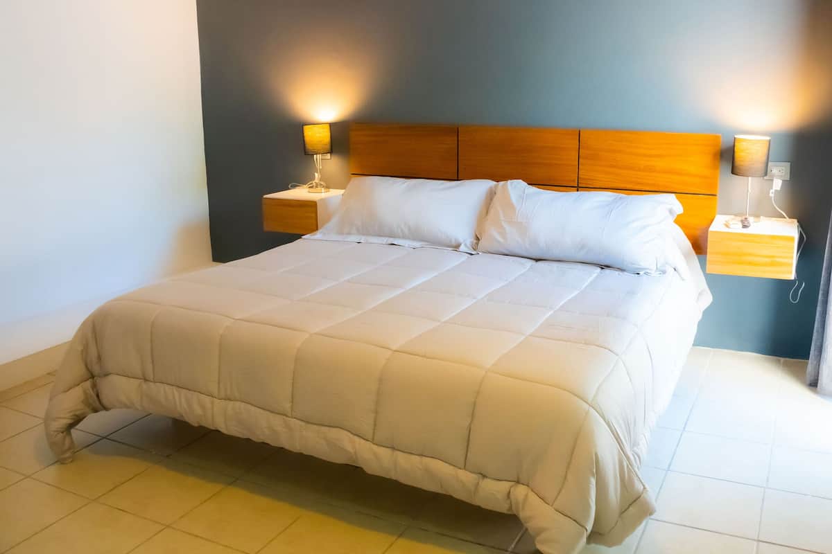 Una cama grande con cabecera de madera y ropa de cama blanca en una habitación de hotel.