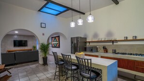 Une cuisine moderne dotée d’un îlot central, de tabourets de bar, d’un réfrigérateur, d’un four à micro-ondes et d’un coin repas avec un téléviseur et des sièges.