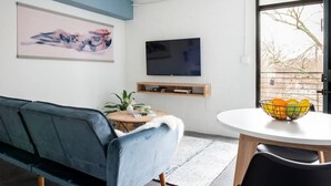 A modern living room with a sofa, a coffee table, a TV, and a window with a view. - *NEW* The Jolene - Walkable | Ponce City (Atlanta)
