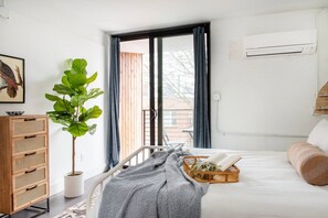 Ein Schlafzimmer mit einem Bett, einem Nachttisch, einer Zimmerpflanze, einem Fenster mit Vorhängen und einer Klimaanlage.