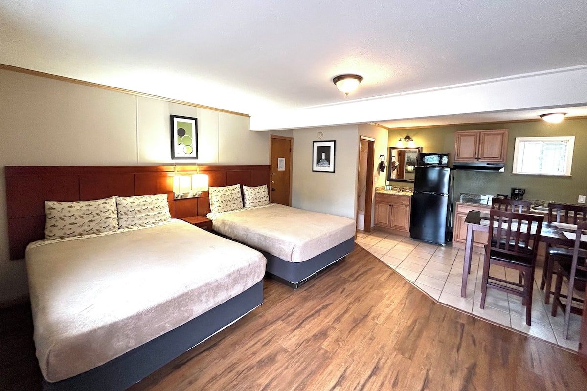 A hotel room with two beds, a kitchenette, and a dining area.