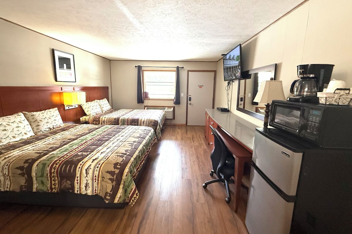 A hotel room with two beds, a desk with a microwave, a coffee maker, and a TV.