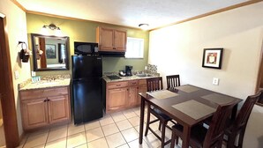 A compact kitchen with wooden cabinets, a black refrigerator, a microwave, a sink, and a dining table with chairs.
