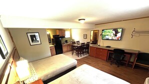 A compact room with a bed, a desk, a chair, a television, and a kitchenette.