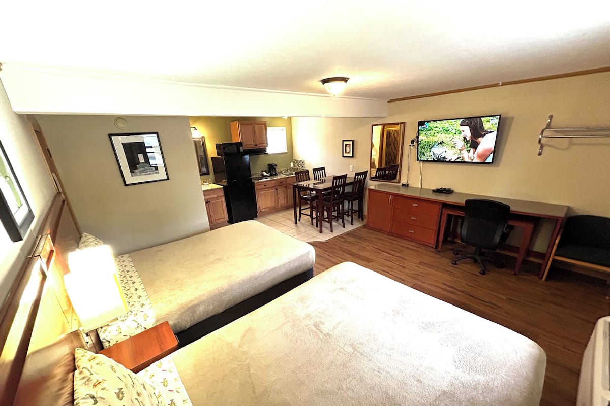 A compact room with a bed, a desk, a chair, a television, and a kitchenette.