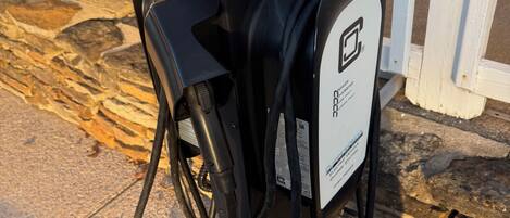 A portable gas pump with a warning sign, connected to a bicycle, on a concrete surface near a white fence.