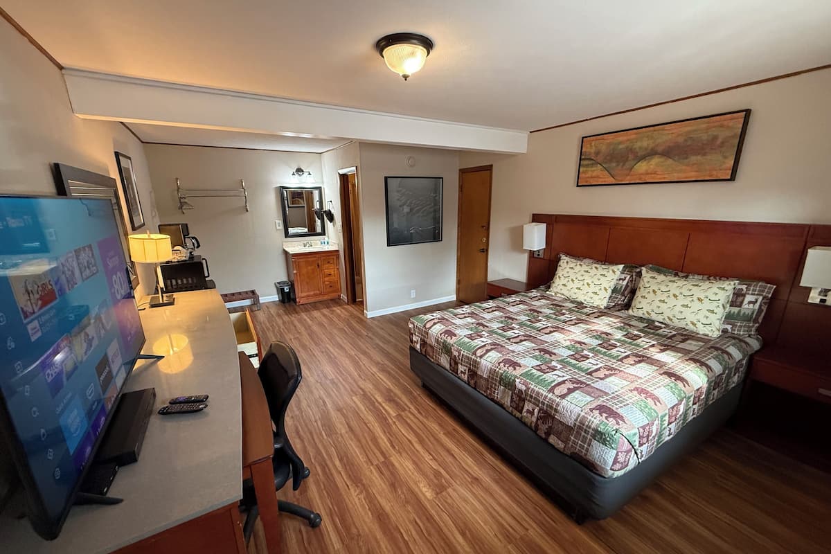 A hotel room with a bed, desk, chair, TV, and a painting on the wall.