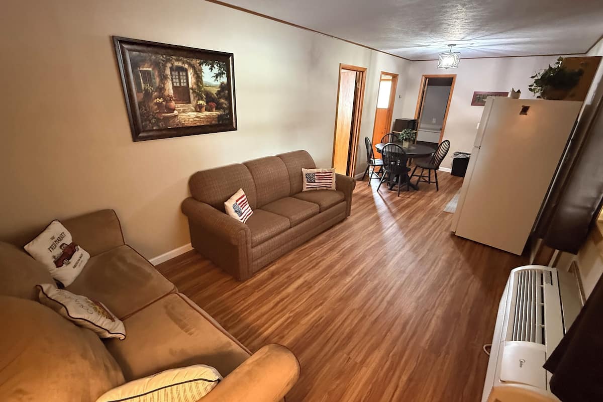 A living room with a brown sofa, a dining table with chairs, and a kitchen area with a refrigerator.