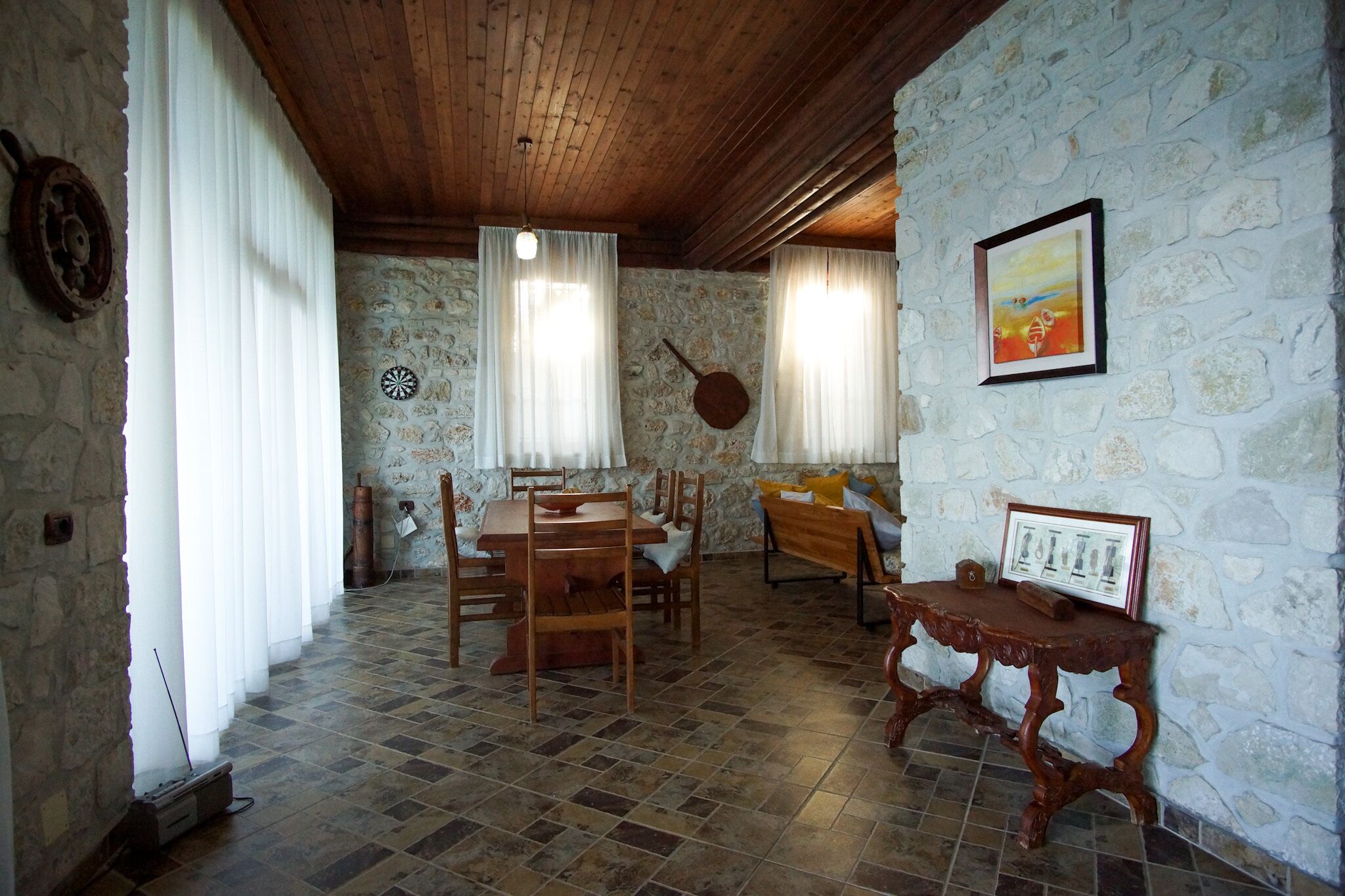 A dining area with a wooden table and chairs, stone walls, and a rustic ceiling.