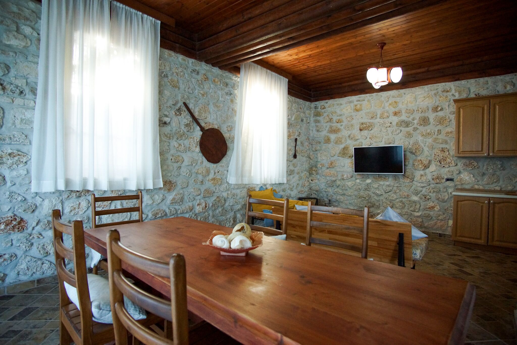 Un coin repas rustique avec un mur en pierre, un plafond en bois et une table en bois, agrémentée de chaises.
