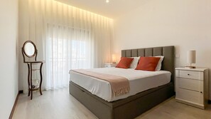 A bedroom with a bed, bedside table, lamp, and a mirror.
