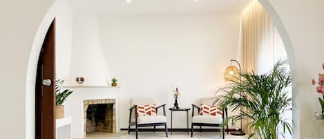 A living room with a fireplace, two armchairs, a coffee table, and a large plant.
