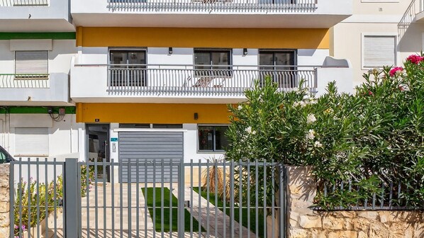 Un edificio residencial de varios pisos con balcones, un acceso cerrado y un jardín bien cuidado.
