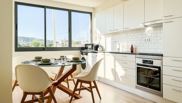 Una cucina moderna con mobili bianchi, un tavolo da pranzo in vetro e vista sull'esterno.