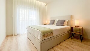 Una camera da letto con un letto, due comodini, una lampada e una finestra con tende leggere.