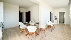 Un'area pranzo moderna con tavolo in vetro, sedie bianche e pavimento in legno.