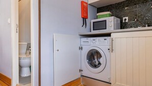 Een kleine wasruimte met een wasmachine, een magnetron en een toilet.