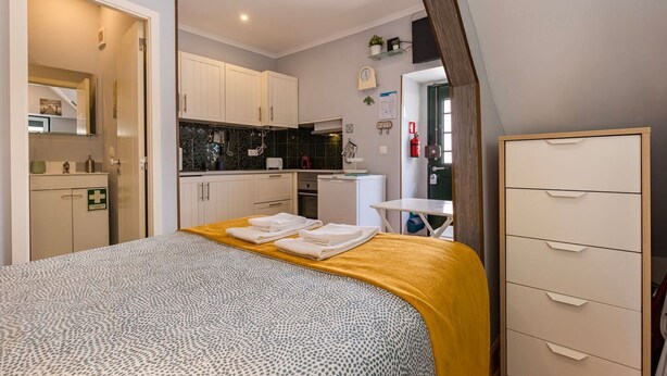 Een compacte hotelkamer met een bed, een kleine keuken, een bureau en een kledingkast.
