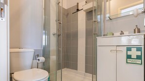 Een badkamer met een douchecabine van glas, een toilet en een kastje met een verbandtrommel-pictogram.