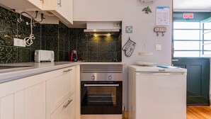 Een kleine keuken met witte kastjes, een inbouwoven, een koelkast en een magnetron.