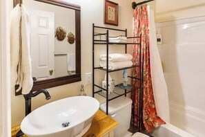 Un baño con lavamanos blanco, un espejo, repisas con toallas y una cortina de ducha.