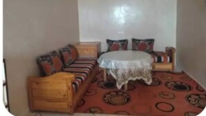 A room with a wooden sofa set, a small round table with a lace tablecloth, and a patterned carpet.