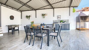 An outdoor patio with a dining table and chairs, a foosball table, and a kitchen area with a grill.