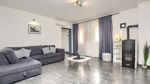 A modern living room with a grey sofa, a round coffee table, a fireplace, and a large window with curtains.