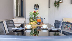 A breakfast table with fruits, a coffee pot, and a jar of orange juice, set in a modern room with metal chairs and a dartboard on the wall.
