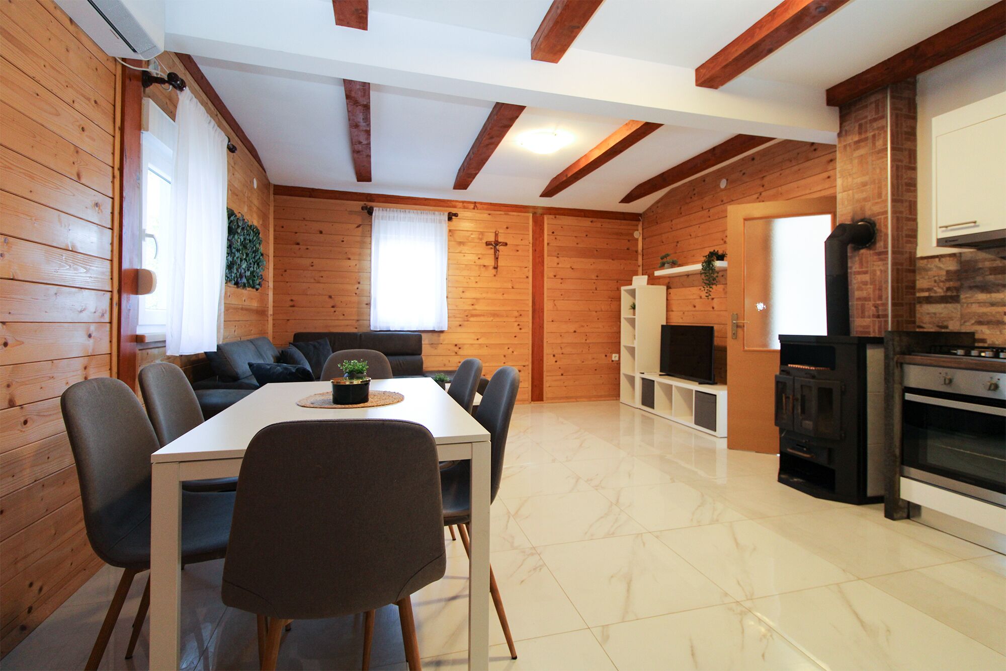 Een houten interieur met een eettafel, stoelen, een bank, een televisie en een open haard.