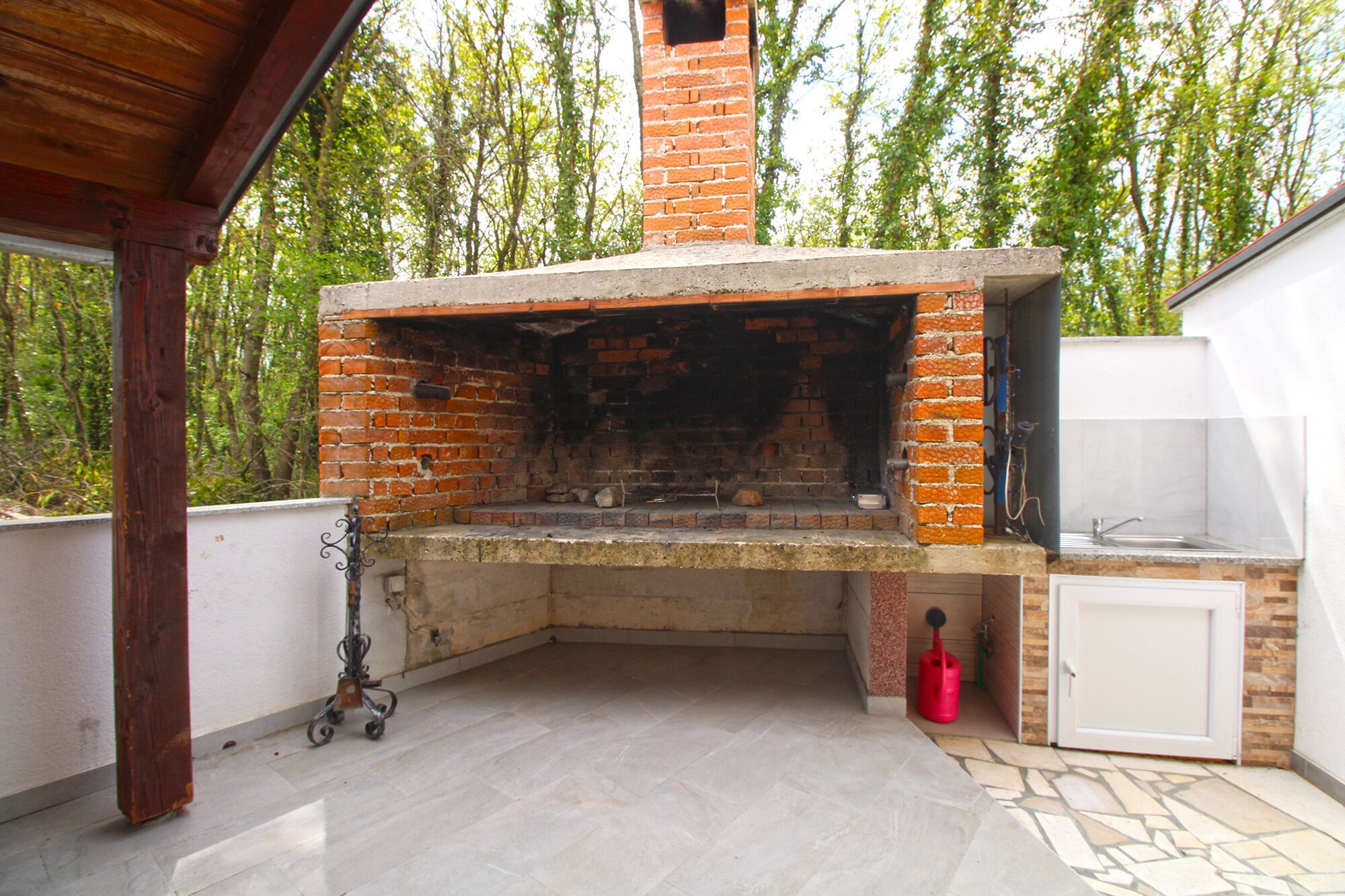 An outdoor brick oven with a stone countertop, a sink, and a red bucket.