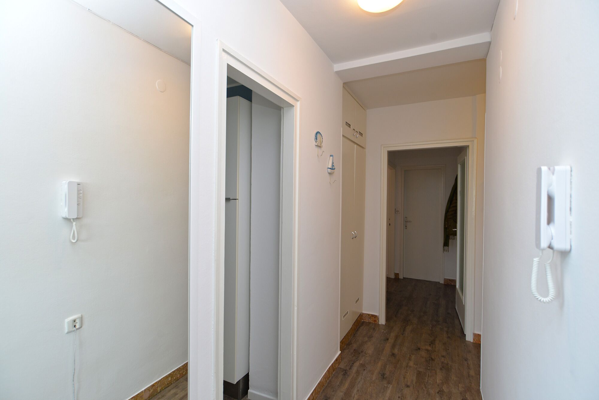 A hallway with white walls, a wooden floor, and two phones mounted on the walls.