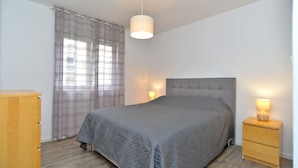 Une chambre à coucher comprenant un lit, deux tables de chevet avec des lampes, une commode en bois et une fenêtre avec des rideaux.