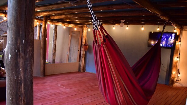 Un'amaca in una stanza in legno con pavimento rosso, travi a vista e luci decorative.