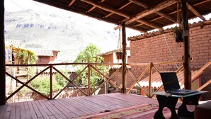 Un patio in legno con un laptop su un tavolo, un tappeto decorato e, sullo sfondo, vista su una montagna e degli edifici.